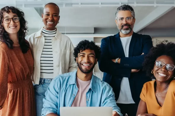 A group of five diverse individuals smiling and posing together in an office setting.