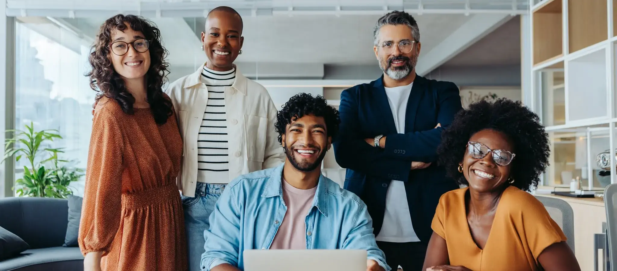 A group of five diverse individuals smiling and posing together in an office setting.